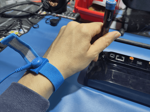 A left hand holding a screwdriver with a blue antistatic wristband on it.