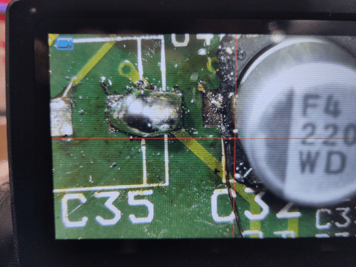 A top down photo taken with the microscope. A capacitor is soldered down and there's a very thin copper wire connected to it, leading off screen.