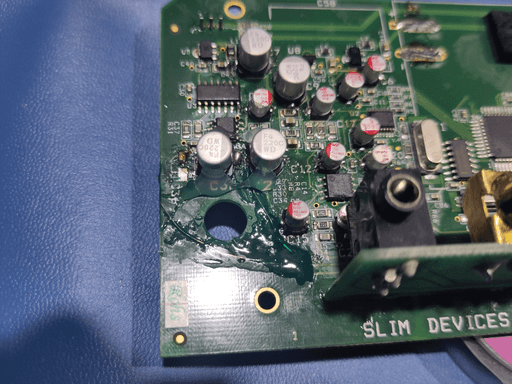 Photo of the motherboard. Two capacitors are secured with two dabs of translucent-white hot glue each. There's also some dark green solder mask covering up the thin copper wires.