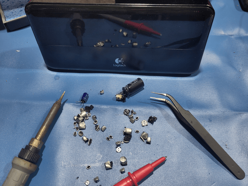 A photo of the Squeezebox Classic put back together. A soldering iron, tweezers, the tip of a multimeter probe and the butchered capacitors are sitting in front of it. They reflect int the glossy front panel of the squeezebox.