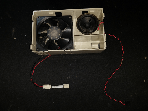 A plastic assembly holding a speaker and a fan. Both are very dusty.