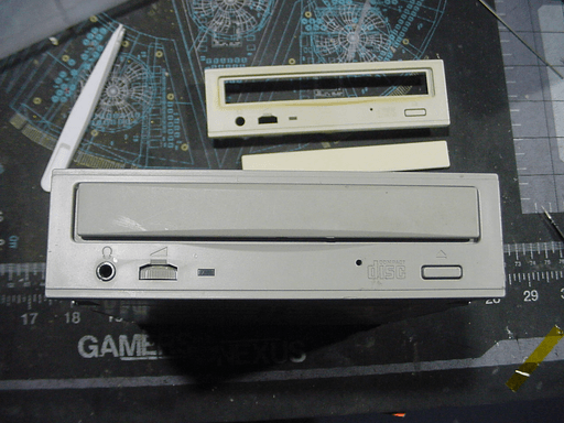 A cd drive with a gray front standing upright next to beige-colored front panel components.