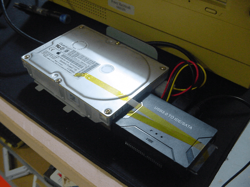 A old hard drive plugged into a USB adapter. The adapter is held to the drive with some tape.