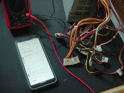 A photo with a multimeter, a PC power supply and a phone showing the pinout of the PSU.