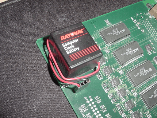 A rectangular battery sitting on top of a pcb with its cable wrapped around it.