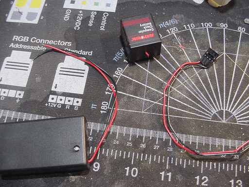 A rectangular battery with it cable cut off and a battery holder next to it.