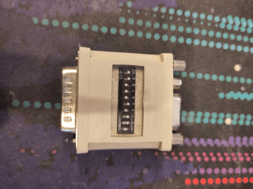 A mac video adapter with a DB-15 connector on one side and a VGA connector on the other. There's a row of ten dip-switches in the middle.