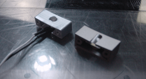 A photo of two small, gray and rectangular plastic pieces. One has cables sticking out from the bottom.