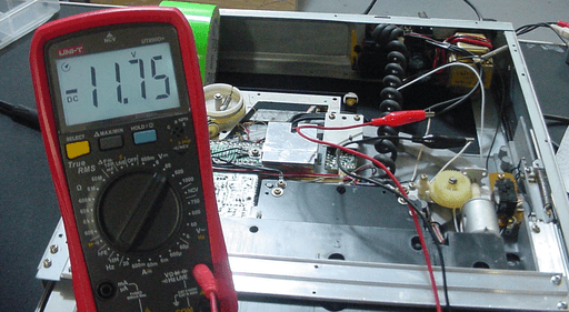 A photo of a multimeter displaying -11.75V. The two alligator clips connected to it clip to two white wires inside the record player.