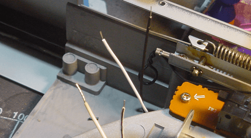 A photo of the wires for the new LED sticking trough a hole into the underside of the record player. There's another set of wires to the left of them.