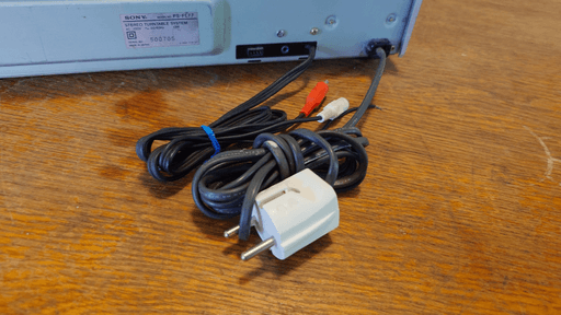 The backside of the record player. The hard-mounted power cable on the back is black with a white plug. It's likely not original.