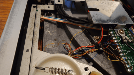 A zoomed-in section of the inside of the record player in question. There's a bundle of wires coming in from under a plastic piece. Some of the wires from that bundle hang loose around inside of the case.